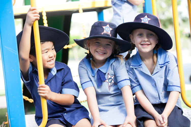 Three young students in school uniform and wide‑brim hats sitting together on playground equipment.