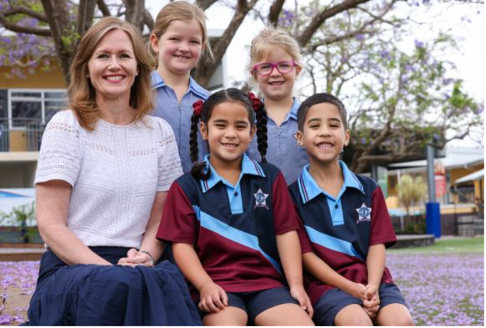 Adult and students seated together outdoors on school grounds.