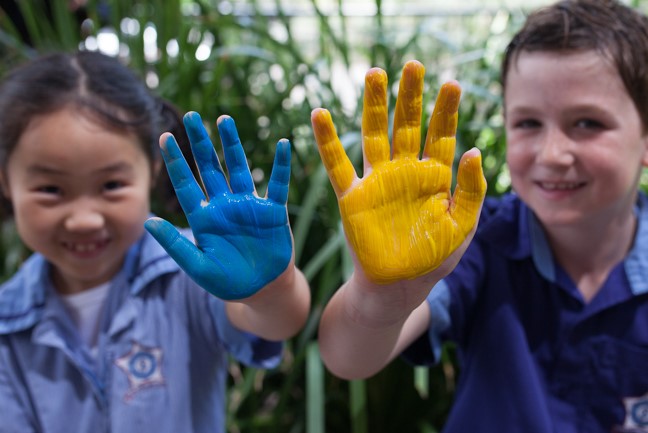 Students showing paint‑covered hands during a school art activity.