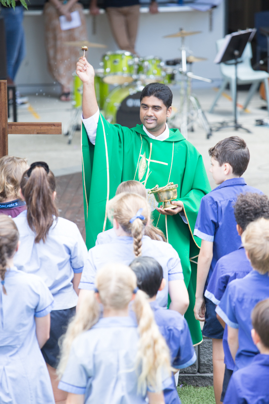 School liturgy taking place outdoors with a religious leader and students gathered together.