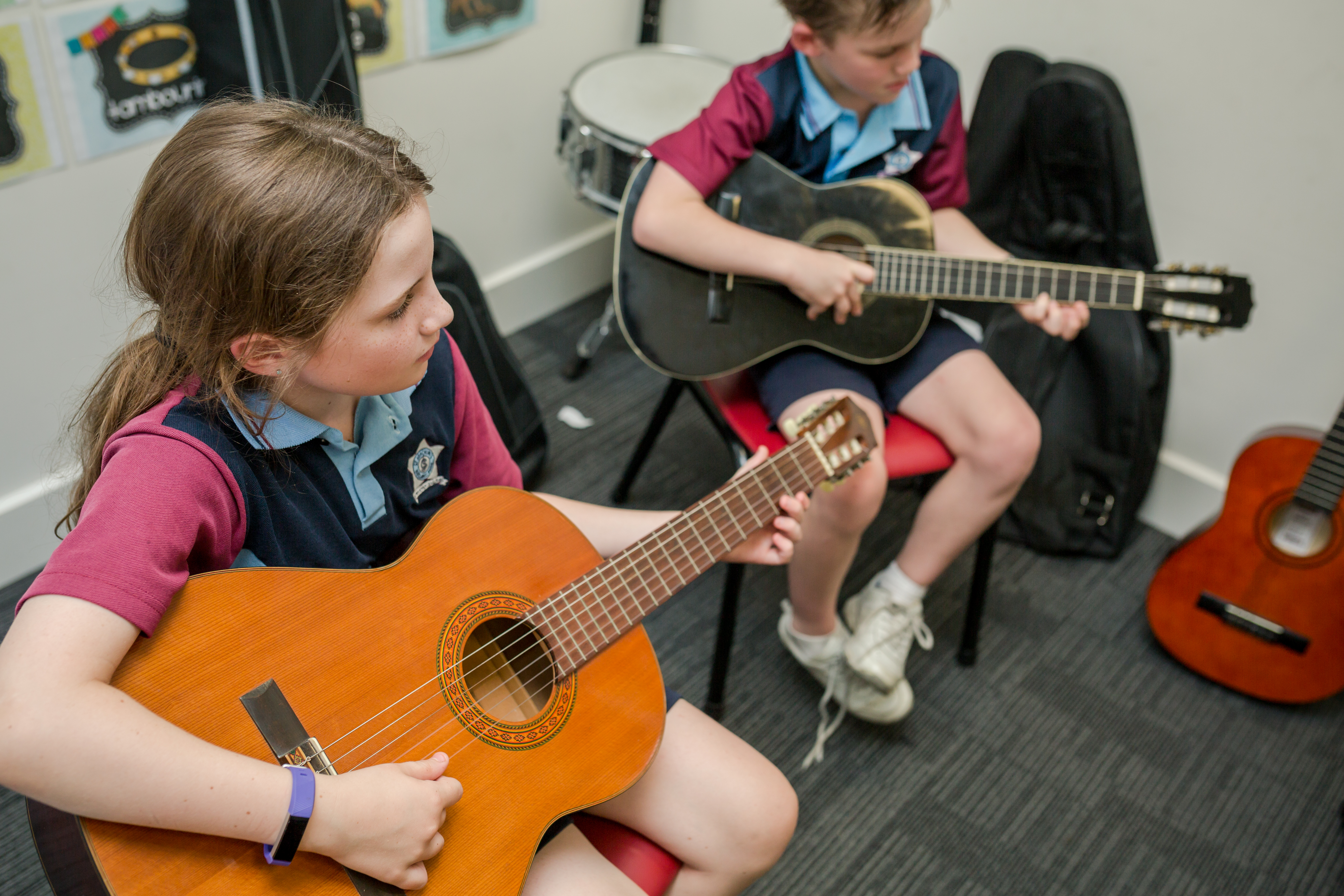Two students sitting down playing guitar.
