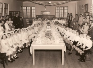 Archival photograph of a large school or community gathering seated at a long table.