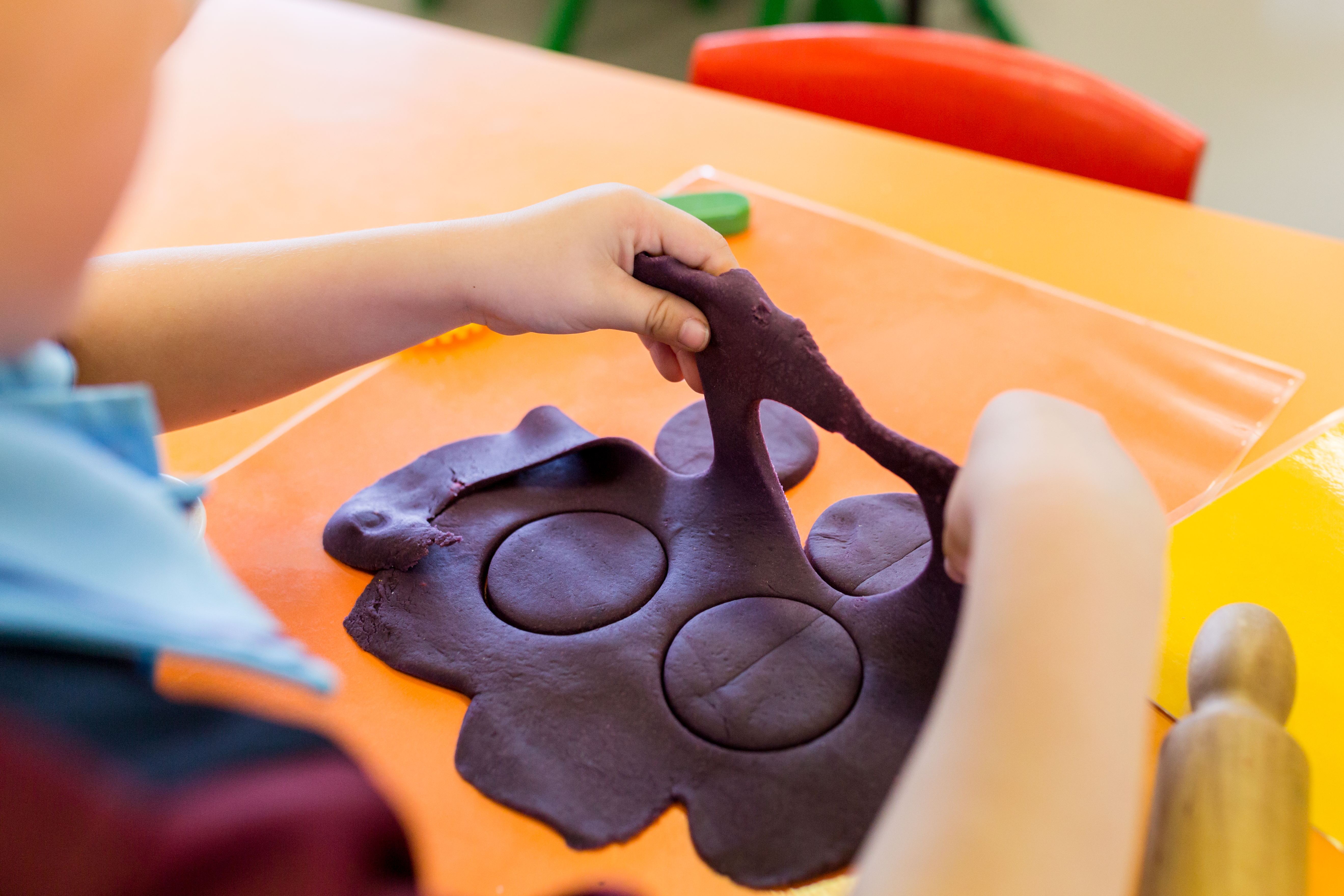 Student stretching and shaping purple playdough on a table during a hands‑on classroom activity.